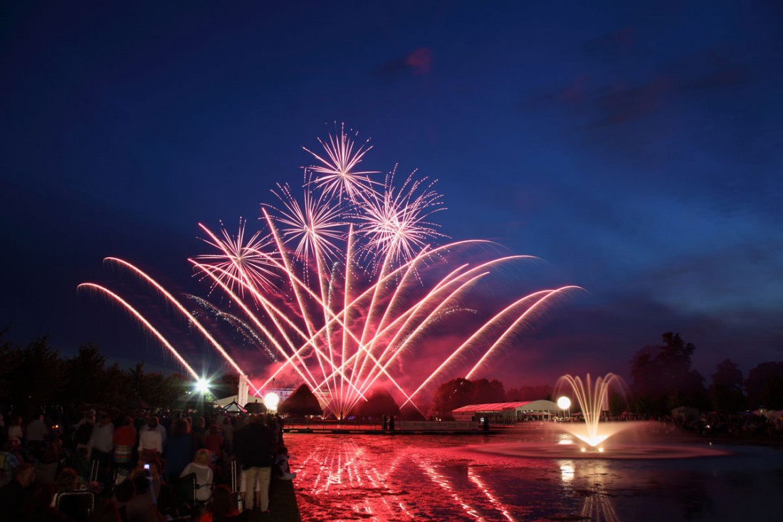 Red and pink fireworks reflected in the long water at Hampton Court Palace
