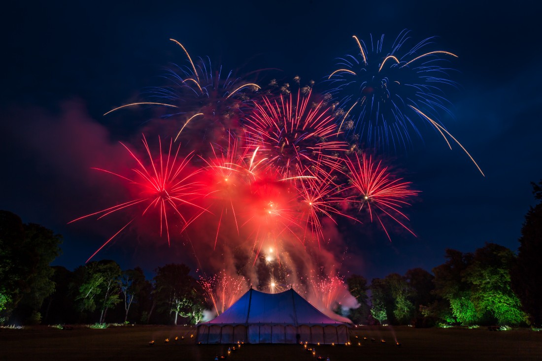 Red and blue fireworks bursting in the skies above a marquee in Scotland
