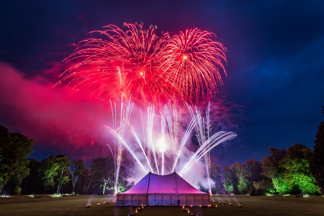 Big red fireworks burst above silver fireworks behind a marquee in Scotland