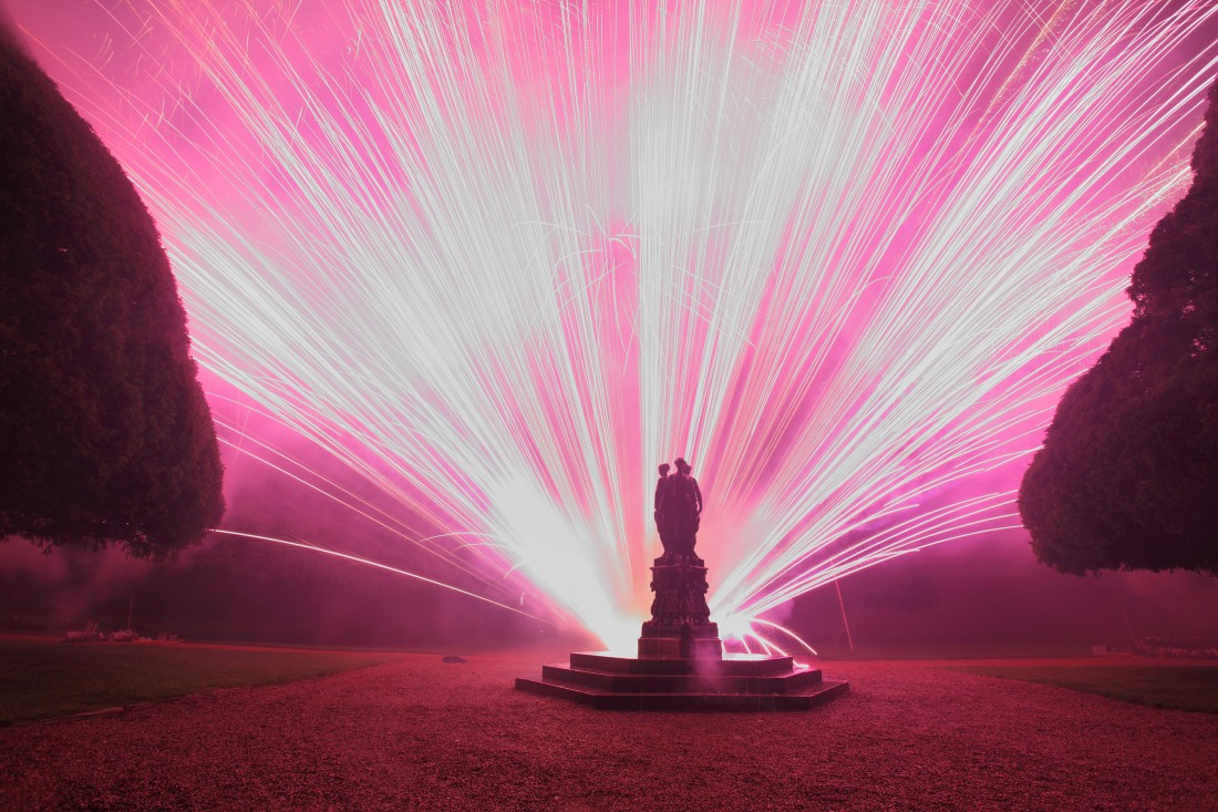 Fan of bright pink fireworks with a statue in the foreground at Hampton Court Palace