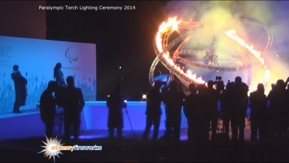 Young female paralympian surrounded by flames and pyrotechnics at the Paralympic torch lighting ceremony